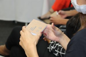 detalhe de mãos de uma mulher, unhas pintadas de vermelho, folheando um pequeno bloco de anotações impresso com a nova marca da Fundep Concursos.